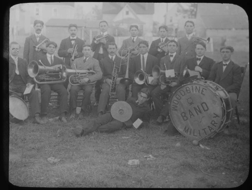 Stara fotografia: kilkunastu muzyków w mundurach z instrumentami dętymi blaszanymi, z przodu bęben wielki z napisem
